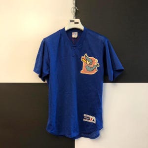 May include: A royal blue baseball jersey with a mesh design. The jersey features a cartoon bird logo holding a baseball bat on the chest. It has a button-up front and short sleeves. A Majestic Apparel tag is visible.