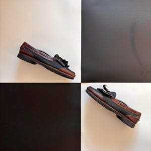 May include: A pair of brown and black leather loafers with tassel detailing. The shoes feature a classic design with a dark sole, set against a black and white chequered background. These loafers are a stylish footwear choice.