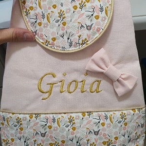 May include: Pink fabric backpack with a floral pattern and a gold embroidered name "Gioia".