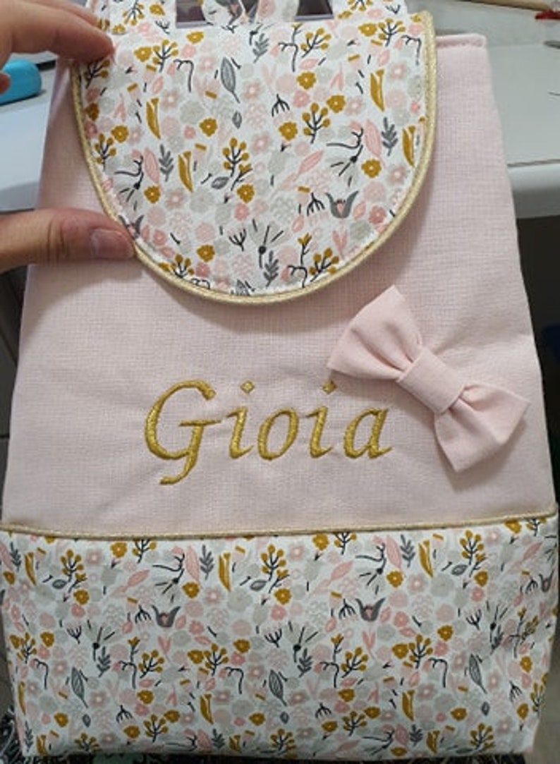 May include: Pink fabric backpack with a floral pattern and a gold embroidered name "Gioia".