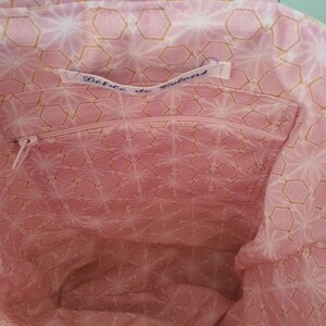 May include: The inside of a pink fabric tote bag with a gold geometric pattern. The bag has a zippered pocket with a label that reads "DeFute de Colons".