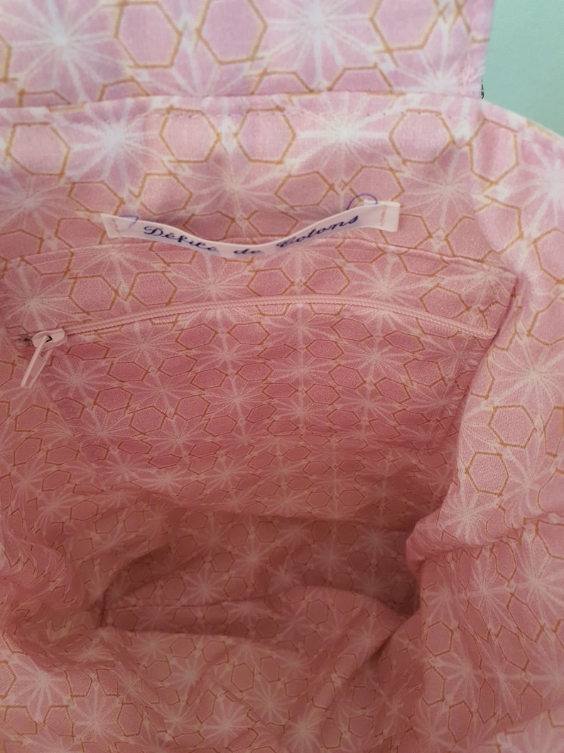 May include: The inside of a pink fabric tote bag with a gold geometric pattern. The bag has a zippered pocket with a label that reads "DeFute de Colons".