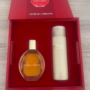 Könnte beinhalten: Ein Giorgio Armani Sensi Geschenkset in einer roten Box. Das Set enthält einen Parfümflakon und eine Körperlotion. Der Parfümflakon ist oval mit einem goldenen Verschluss. Die Körperlotion ist eine hohe, weiße Flasche.