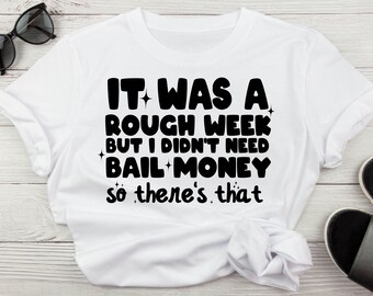 May include: White t-shirt with black text that reads "It was a rough week but I didn't need bail money so there's that."