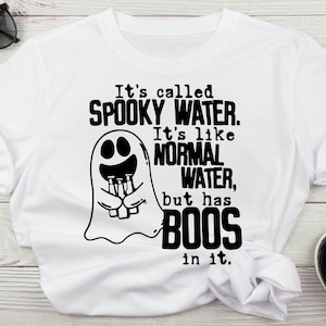 以下が含まれることがあります： 白いTシャツに、ビール瓶を持った幽霊の白黒のグラフィックが描かれています。テキストには「It's called SPOOKY WATER. It's like NORMAL WATER, but has BOOS in it.」と書いてあります。