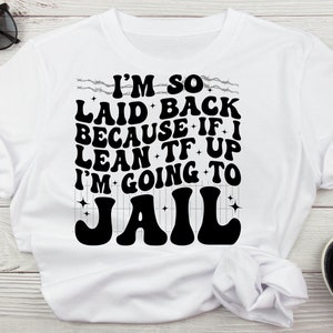 May include: White t-shirt with the text "I'M SO LAID BACK BECAUSE IF I LEAN TF UP I'M GOING TO JAIL" in a retro font. The graphic is in black. Black sunglasses and sandals are visible.