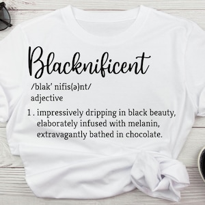May include: White t-shirt with a black graphic design that reads "Blacknificent" and defines the word as "impressively dripping in black beauty, elaborately infused with melanin, extravagantly bathed in chocolate."