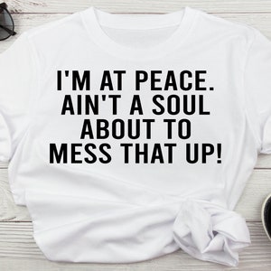 May include: White t-shirt with black text that reads "I'm at peace. Ain't a soul about to mess that up!"