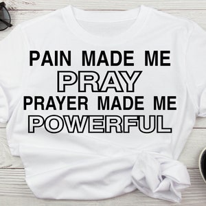 May include: White t-shirt with black text that reads "Pain made me pray, prayer made me powerful."