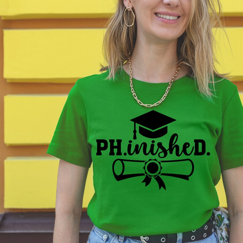 以下が含まれることがあります： 黒い卒業帽と卒業証書のグラフィックと「PH.inished.」というテキストが書かれた緑色のTシャツ