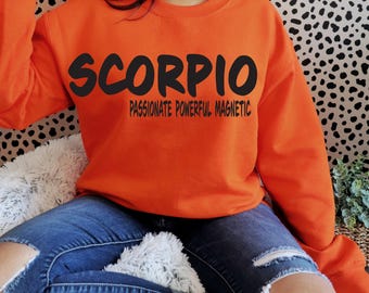May include: Orange sweatshirt with black text that reads "SCORPIO PASSIONATE POWERFUL MAGNETIC".
