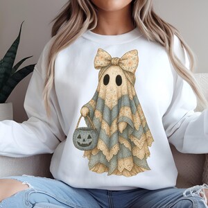Puede incluir: Sudadera blanca con una ilustración en acuarela de un fantasma con un lazo y un cubo de calabaza. El fantasma está adornado con encaje y patrones de chevron en beige y gris. Diseño temático de Halloween.
