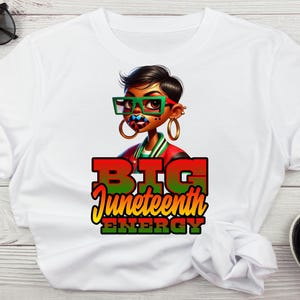 May include: White t-shirt with a cartoon illustration of a Black woman wearing glasses and a red and green jacket. The text "BIG Juneteenth ENERGY" is printed in red, green, and yellow.