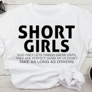 May include: White t-shirt with black text that reads "SHORT GIRLS GOD ONLY LETS THINGS GROW UNTIL THEY ARE PERFECT, SOME OF US DIDN'T TAKE AS LONG AS OTHERS."