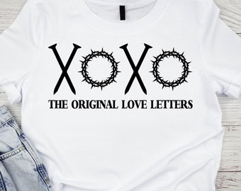 May include: White t-shirt with a black graphic design of two nails forming an 'X' and two crown of thorns forming 'O's. The text 'XOXO THE ORIGINAL LOVE LETTERS' is below the graphic.