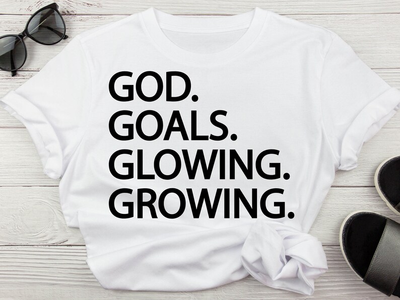 以下が含まれることがあります： 黒い文字で「GOD. GOALS. GLOWING. GROWING.」と書かれた白いTシャツ