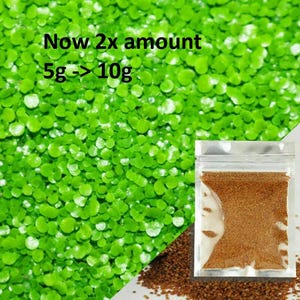 Könnte beinhalten: Nahaufnahme von leuchtend grünen Wasserpflanzen mit dem Text "Now 2x amount 5g -> 10g". Ein kleiner, durchsichtiger Beutel enthält braune Granulate. Ein Teil der braunen Granulate ist ebenfalls sichtbar.