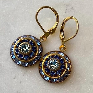 May include: Gold earrings with a blue and gold circular design. The earrings have a small blue crystal in the center of the design.