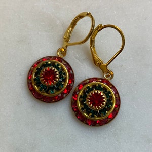 May include: Gold tone earrings with red and green crystal accents. The earrings have a circular design with a smaller red crystal in the center.