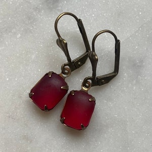 Puede incluir: Un par de pendientes con piedras de vidrio rojo engastadas en metal de tono dorado antiguo.