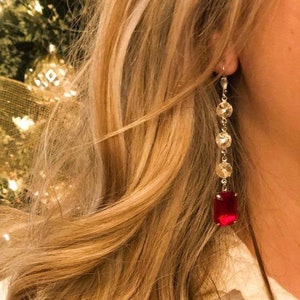 May include: A pair of long, dangling earrings with a red gemstone at the bottom and clear crystal accents.