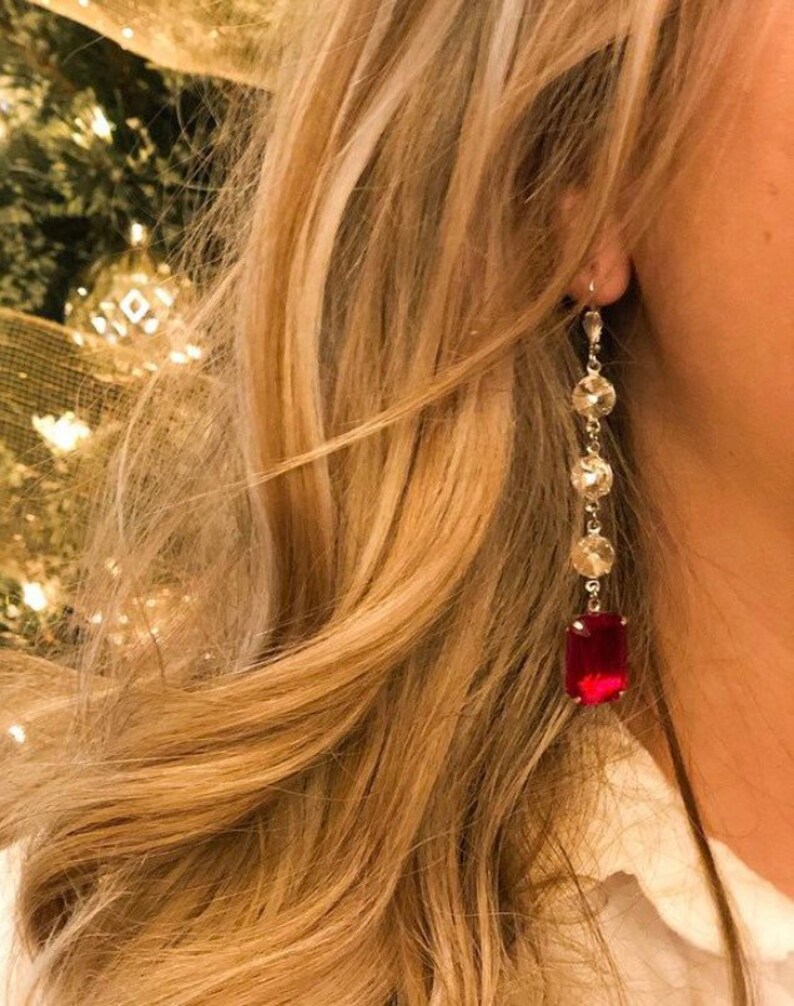 May include: A pair of long, dangling earrings with a red gemstone at the bottom and clear crystal accents.