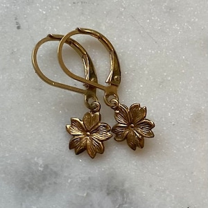 May include: A pair of gold-toned earrings with a delicate flower design. The earrings have a simple hook closure.