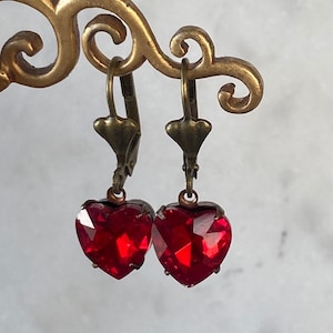 May include: A pair of dangle earrings with red heart-shaped crystals and antique brass hooks.