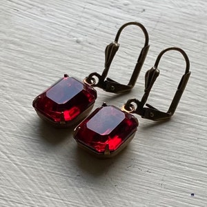 May include: A pair of dangle earrings with red gemstone accents and gold-toned metal hooks.