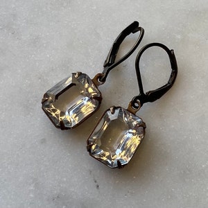 Op de afbeelding: Een paar oorbellen met heldere, gefacetteerde, rechthoekige stenen en zwarte metalen haken.