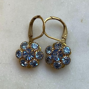 May include: A pair of gold dangle earrings with a flower-shaped design. Each flower has a centre stone and is surrounded by smaller stones. The stones are a light blue colour.