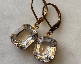 May include: A pair of gold earrings with clear, faceted, emerald-cut crystals hanging from the bottom.