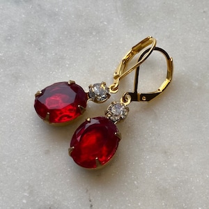 May include: Gold earrings with red and clear oval-shaped stones. The earrings have a lever back closure.