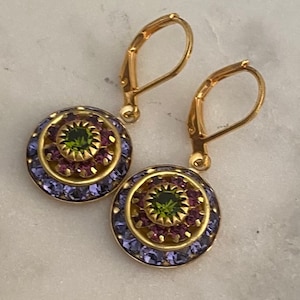 Puede incluir: Pendientes de oro con un diseño redondo multicolor. Los pendientes presentan una piedra central verde rodeada de piedras moradas y rosas.