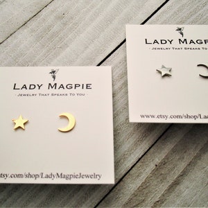 May include: Two pairs of gold and silver earrings on a white card. The earrings are a star and a crescent moon. The card has the text "Lady Magpie - Jewelry that speaks to you - www.etsy.com/shop/LadyMagpieJewelry"