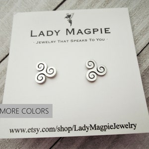 May include: A pair of silver earrings with a triple spiral design. The earrings are on a white card with the text "Lady Magpie Jewelry That Speaks To You" and "More Colors" printed on it. The website address "www.etsy.com/shop/LadyMagpieJewelry" is also printed on the card.