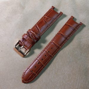 May include: Two brown leather watch straps with a crocodile pattern. One strap has a gold buckle.
