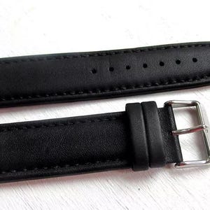 May include: A black leather watch strap with a silver buckle. The strap is stitched and has a smooth, textured surface.