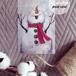 May include: Watercolor painting of a snowman with a red scarf and a carrot nose. The snowman has a happy expression and is standing with its arms outstretched. The painting is on a white background and has a "Bestseller print card" label in the top right corner.