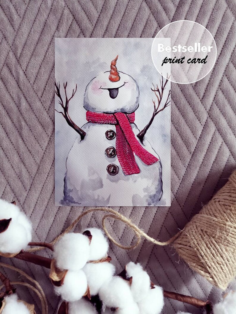 May include: Watercolor painting of a snowman with a red scarf and a carrot nose. The snowman has a happy expression and is standing with its arms outstretched. The painting is on a white background and has a "Bestseller print card" label in the top right corner.