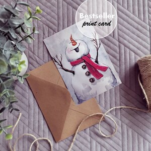 May include: A watercolor illustration of a snowman with a red scarf and buttons. The illustration is printed on a white card with the text "Bestseller print card" in a circle.
