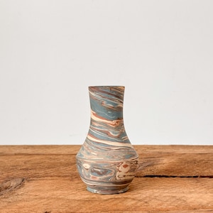 May include: A small, decorative vase with a unique marbled design. The vase features a blend of blue, brown, and cream colours, creating a swirling pattern. The vase is approximately 15 cm tall and has a rounded base and a narrow neck.