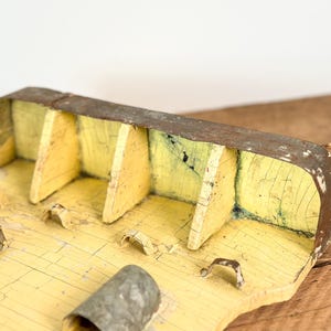K&ouml;nnte beinhalten: Eine verwitterte Holzkiste mit gelb lackiertem Innenraum und rostiger Metallau&szlig;enseite. Die Kiste hat mehrere F&auml;cher und eine kleine Schlaufe an der Seite. Die Farbe ist rissig und verleiht ihr ein rustikales Aussehen.