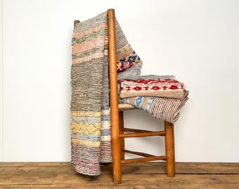 Könnte beinhalten: Ein Holzstuhl mit einem Stapel farbenfroher, gestreifter gewebter Textilien. Die Textilien weisen rote, blaue, gelbe und neutrale Farbtöne auf. Der Stuhl ist aus hellem Holz gefertigt und steht auf einer Holzoberfläche.