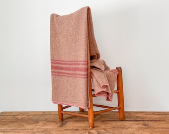 Könnte beinhalten: Eine braune Decke mit roten Streifen, die über einem Holzstuhl drapiert ist. Die Decke hat ein strukturiertes Aussehen und ist über der Rückenlehne und dem Sitz des Stuhls gefaltet. Der Stuhl ist aus Holz und hat ein schlichtes Design.