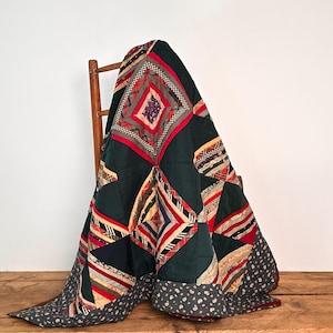 May include: A patchwork quilt featuring a dark green base with diamond-shaped patterns composed of multi-colored striped, plaid, and floral fabric strips. The quilt has a dark gray border with a small white floral print along the bottom edge.