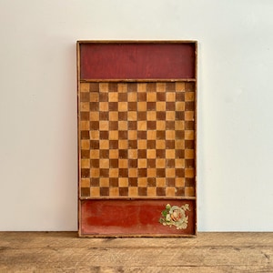 May include: A vintage wooden game board with a checkerboard pattern in brown and tan. The board has a red painted border and a red painted bottom section with a floral design.
