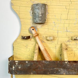 K&ouml;nnte beinhalten: Ein antiker Wandorganizer mit abgenutzter gelber Oberfl&auml;che. Er verf&uuml;gt &uuml;ber Metallbeh&auml;lter, einen h&ouml;lzernen Nudelholz und ein rostiges Metallregal. Das Holz hat einen Risslackeffekt, der seinen Vintage-Charme unterstreicht.