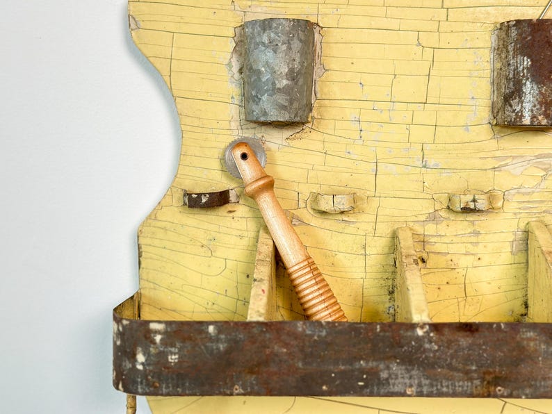 K&ouml;nnte beinhalten: Ein antiker Wandorganizer mit abgenutzter gelber Oberfl&auml;che. Er verf&uuml;gt &uuml;ber Metallbeh&auml;lter, einen h&ouml;lzernen Nudelholz und ein rostiges Metallregal. Das Holz hat einen Risslackeffekt, der seinen Vintage-Charme unterstreicht.