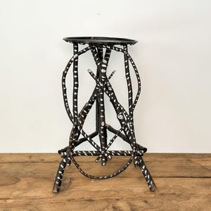 May include: A black metal plant stand with a round top and a base. The stand's legs are made of curved metal rods, decorated with white dots. The stand is approximately 61 cm tall.